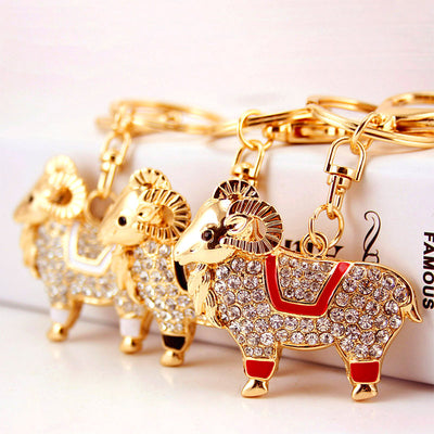 Three gold-tone ram keychains with red, black, and white enamel details stand together.