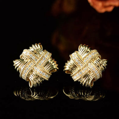Gold woven cross knot stud earrings pair on black reflective surface