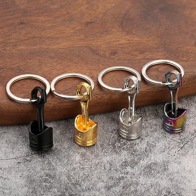 Four piston-shaped keychains in black, gold, silver, and rainbow finishes.