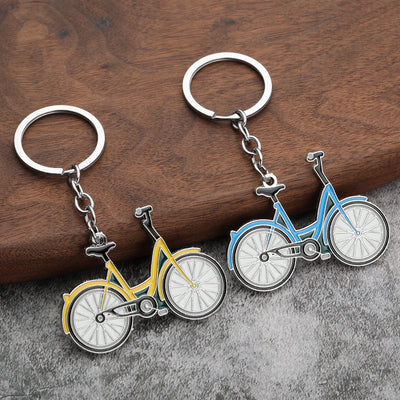 Yellow and sky blue bicycle keychains rest on a wooden and gray fabric surface.