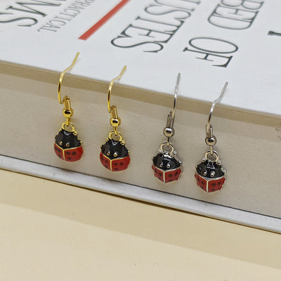Two pairs of mini enamel ladybug earrings with gold and silver hooks on book edge