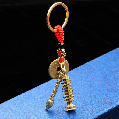 Antique gold-tone coin, brush, and pagoda charms hanging from a red cord key ring.