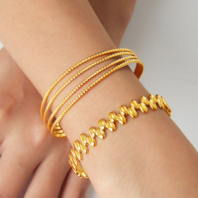 Gold quad textured cuff and oval bead open bangle worn on wrist