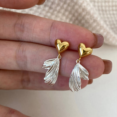 Gold heart stud silver wing drop earrings held in hand