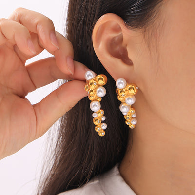 Model holding gold pearl cluster drop earring near ear