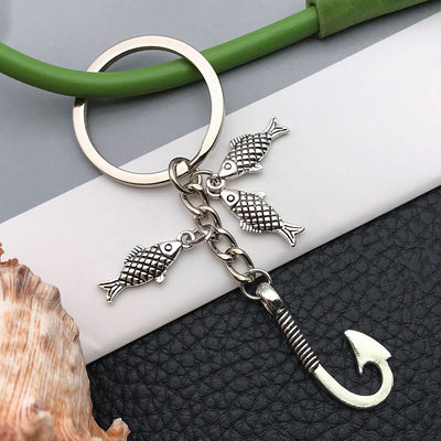Front product photo of antique silver angler fish and hook charm keychain showing the pictured design arrangement