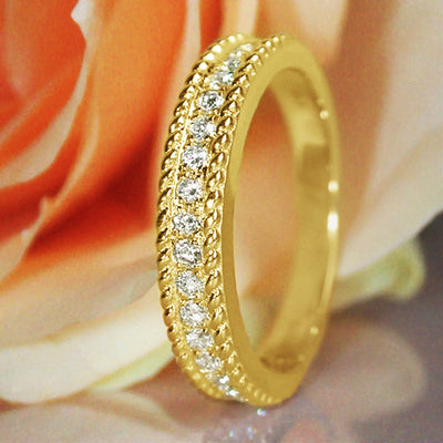 Gold rope-edge clear CZ channel band ring upright on rose petals