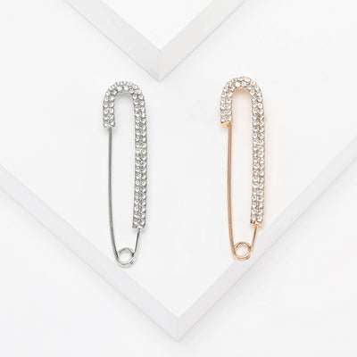 Silver and gold rhinestone safety pin brooches on white steps