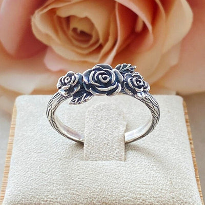 Antique silver three-rose ring on display with rose