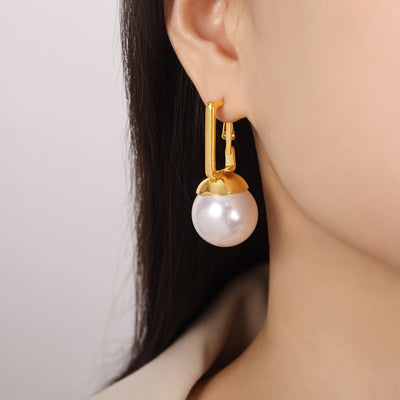 Gold square frame white ball drop earring worn on ear