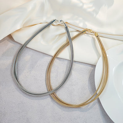 Gold and silver multi-strand snake chain chokers on fabric with white dish