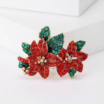 Front product view of the red crystal flower and green leaf cluster brooch on a light background