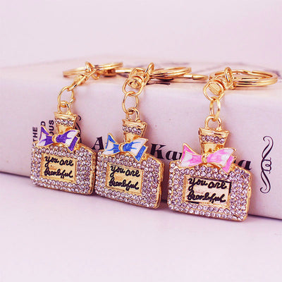Three perfume bottle keychains with purple, blue, and pink bows displayed together.
