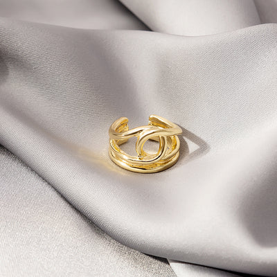 Gold open adjustable crossed band metal ring on gray satin fabric