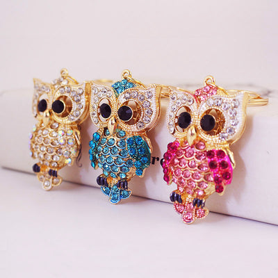 Three gold-tone owl keychains with white, blue, and pink accents.