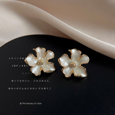 White enamel gold flower studs on black surface with silk