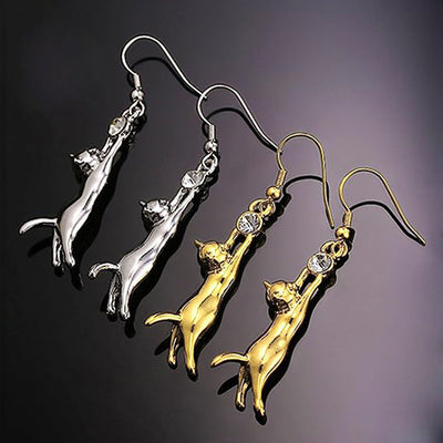 Gold and silver hanging cat earrings on reflective black