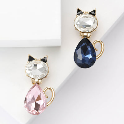 Pink and navy rhinestone cat brooches side by side on white blocks