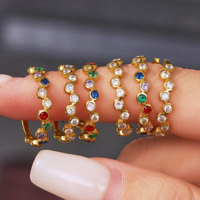 Five gold open band rings stacked on fingers clear and multicolor bezels