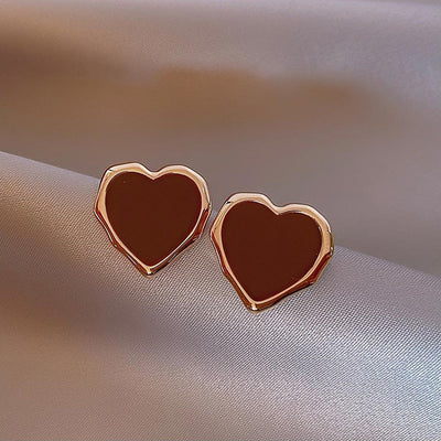 Pair of burgundy enamel heart studs with gold rims on gray satin