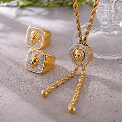 Gold lion head pave rings and rope necklace on textured stone surface