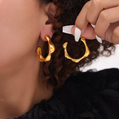 Model wearing and holding gold irregular organic C-shape hoops
