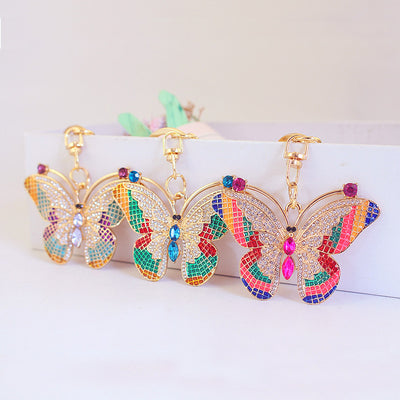 Three gold-tone butterfly keychains with pink, blue, and purple center stones displayed together.
