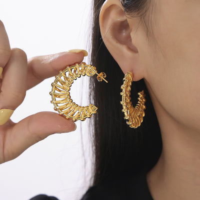 Model holding gold woven C-shape hoop earring next to ear