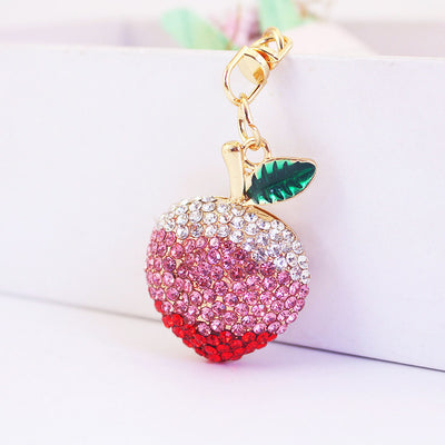 Close-up of a pink and red rhinestone peach charm with a green leaf and gold-tone clasp.
