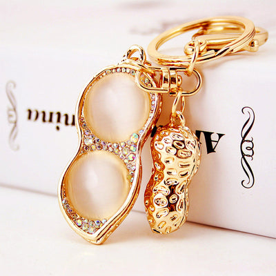Close-up of a gold-tone peanut keychain with cream cabochons and rhinestone trim.