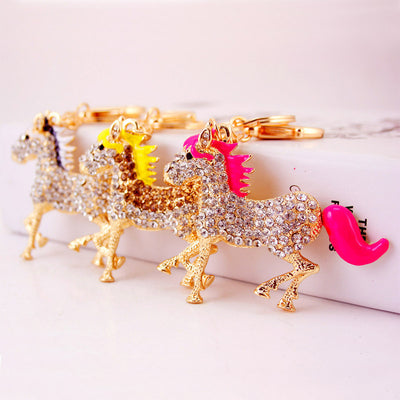 Three gold-tone horse keychains display hot pink, yellow, and pearl white mane and tail colors.
