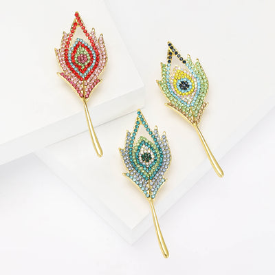 Green Feather, Blue Feather, Red Feather brooch styles arranged on a light display