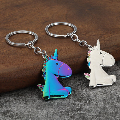White and iridescent unicorn keychains displayed on wood and gray fabric.