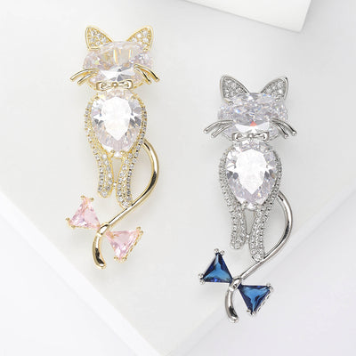 Two colorways of large crystal cat brooch with curled tail and bow accent shown side by side.