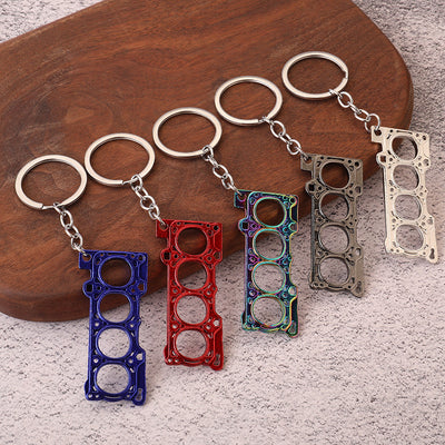 Five engine gasket-shaped keychains in blue, red, iridescent, gunmetal, and silver finishes.