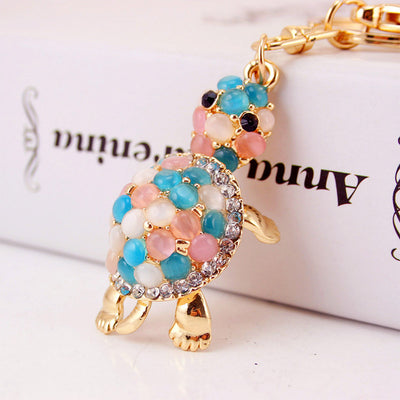 Close-up side view of a turtle charm covered with blue, pink and white stones and clear rhinestone trim.