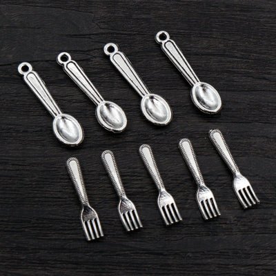 Assorted miniature spoon and fork charms in a silver tone arranged together on a plain background