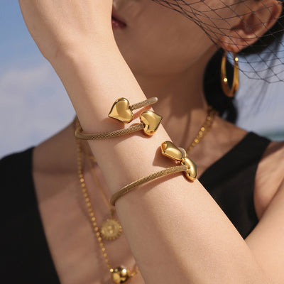 Two gold open heart mesh cuffs stacked on wrist outdoors