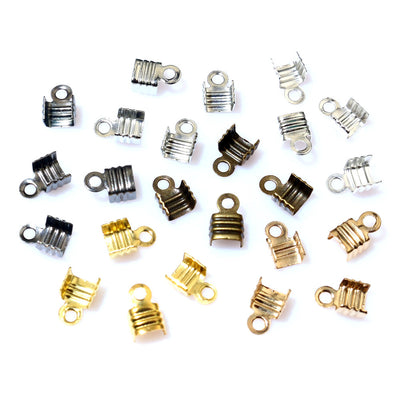 Overview of ridged fold-over cord-end clasps with top loops in three widths and several finishes arranged on a light bac