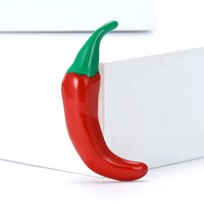 Red enamel chili pepper brooch with green stem upright on white blocks