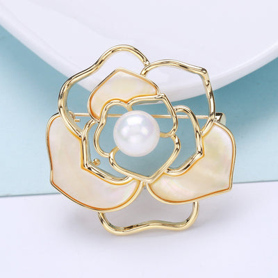 An open gold tone camellia centered by a white pearl shown on a white background.