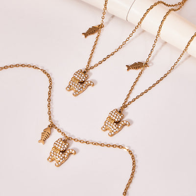 Gold pave cat and fishbone charm necklaces and bracelet on pale surface