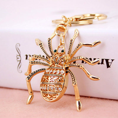 Close view of the gold-tone spider keychain resting against a box on a pink surface.