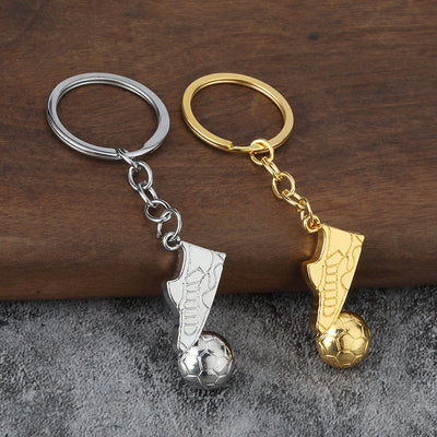 Silver-tone and gold-tone soccer boot keychains arranged together on a wood and gray surface.