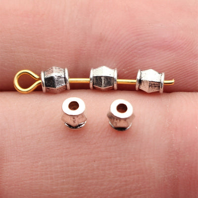 Tiny faceted cube spacer with a centered stringing hole shown close up on a hand