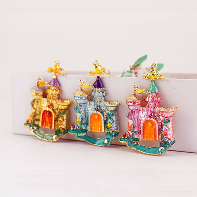 Three raised castle charms in gold, blue, and pink displayed together.