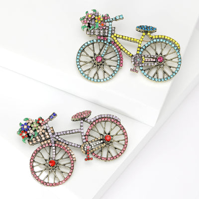 Front view of the crystal bicycle brooch in blue or pink with polished metal detail on a white background