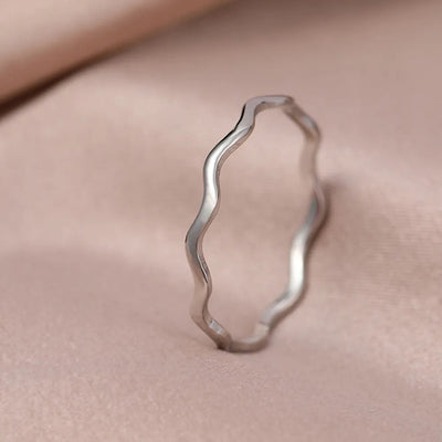 Silver thin wavy band finger ring standing on soft beige fabric
