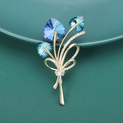 Front view of three-stone crystal bouquet brooch with curled ribbon leaves against a white background.