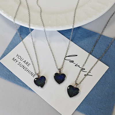 Three silver galaxy glitter heart pendant necklaces on white card blue cloth
